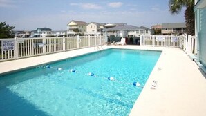 A rectangular swimming pool with clear blue water, surrounded by a white fence.