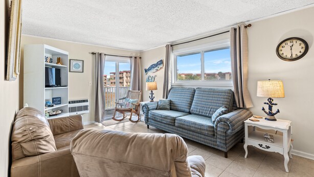A living room with a sofa, a rocking chair, a side table with a lamp, and a wall clock.
