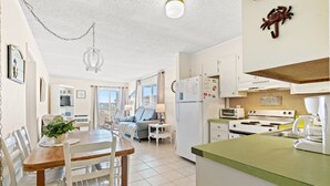 A spacious kitchen with a dining area, a living room with a sofa and a TV, and a view of the city.
