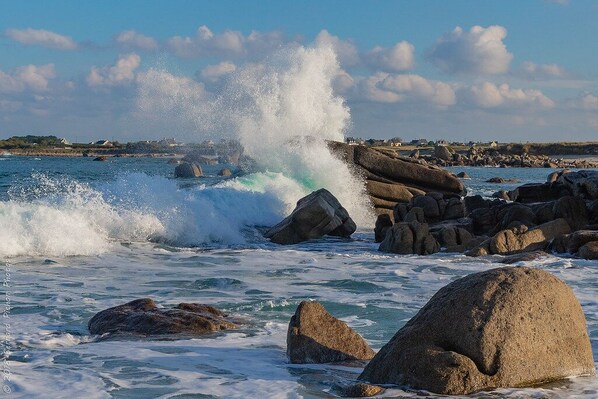 A coastal scene with large rocks and waves crashing against them.