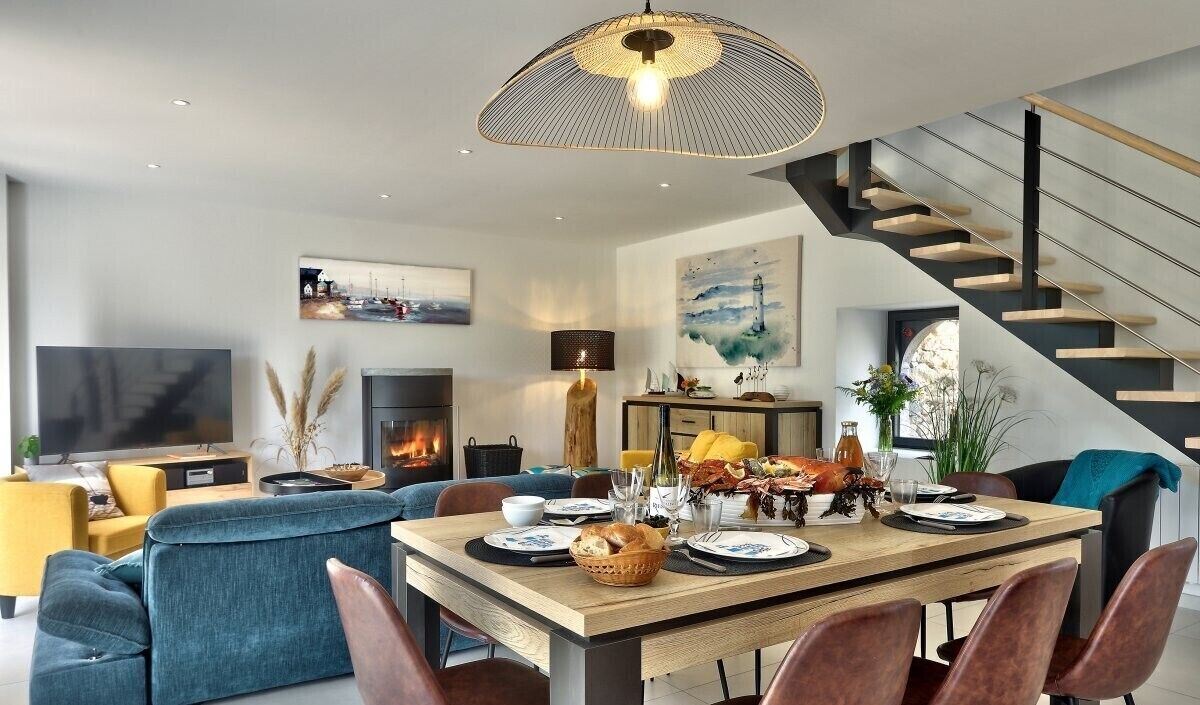Un salon moderne avec une table à manger en bois mise pour le repas, un canapé, un téléviseur et un escalier.