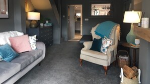 Uma sala de estar com um sofá cinzento, uma poltrona bege e uma mesa lateral de madeira escura.