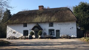 Um pub tradicional com telhado de palha chamado 'The Kings Head', com mesas ao ar livre e fachada de pedra.