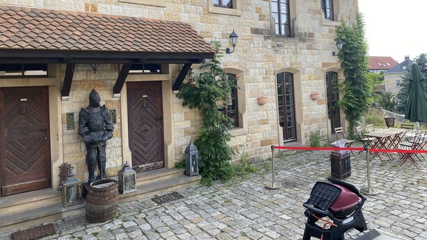 Ein Steinhaus mit mehreren Fenstern und Türen, einem Kopfsteinpflasterhof und Außenbereich mit Sitzgelegenheiten.
