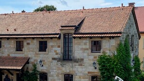 Ein Gebäude aus Stein mit einem Ziegeldach, zahlreichen Fenstern und einer Außenbestuhlung.
