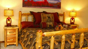 A bed with a wooden headboard, two bedside tables with lamps, a painting of a landscape, and a patterned bedspread.