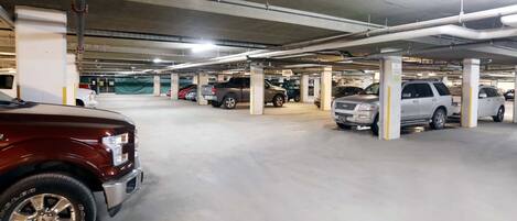 Un estacionamiento subterráneo de varios niveles con pilares de hormigón e iluminación colgante.
