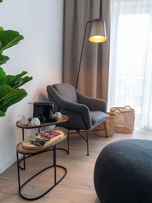 A modern living room with a grey armchair, a coffee table with tea set, a floor lamp, and a large plant. - Limehome Frankfurt Gutleutstraße (Frankfurt)