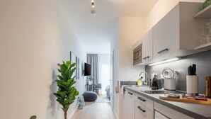 A modern kitchen with a built-in washing machine, a dining area with a grey chair, and a potted plant. - Limehome Frankfurt Gutleutstraße (Frankfurt)