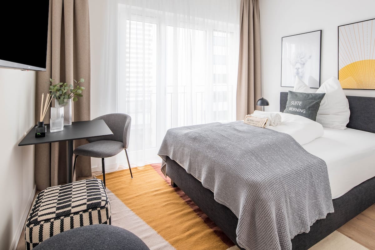 A modern bedroom with a bed, bedside table, chair, and a desk with a lamp.