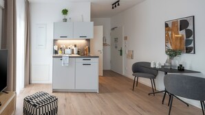 A modern kitchen with white cabinets, a dining area with a gray chair, and a wooden floor. - Limehome Frankfurt Gutleutstraße (Frankfurt)