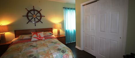 A bedroom with a bed, a ceiling fan, a wooden headboard, a wall-mounted ship's wheel, and a white door.