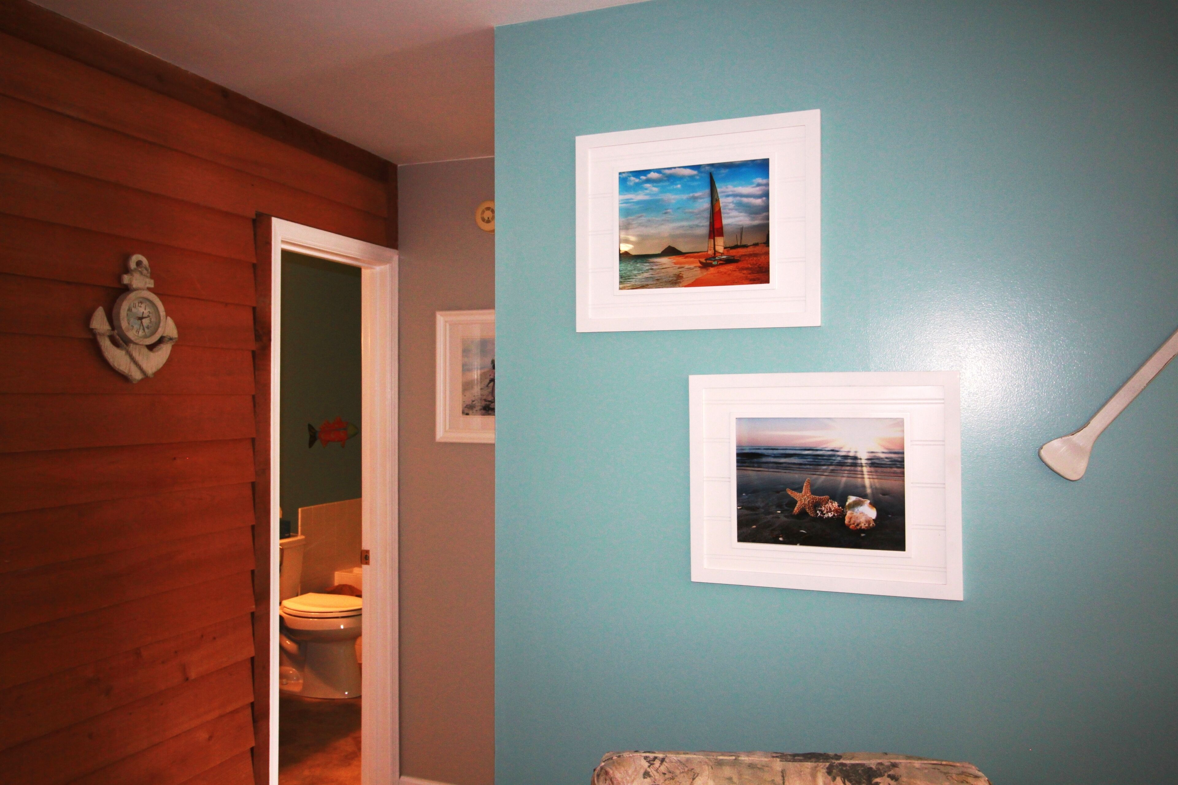 A bathroom with wooden paneling, a toilet, and two framed pictures on the wall.