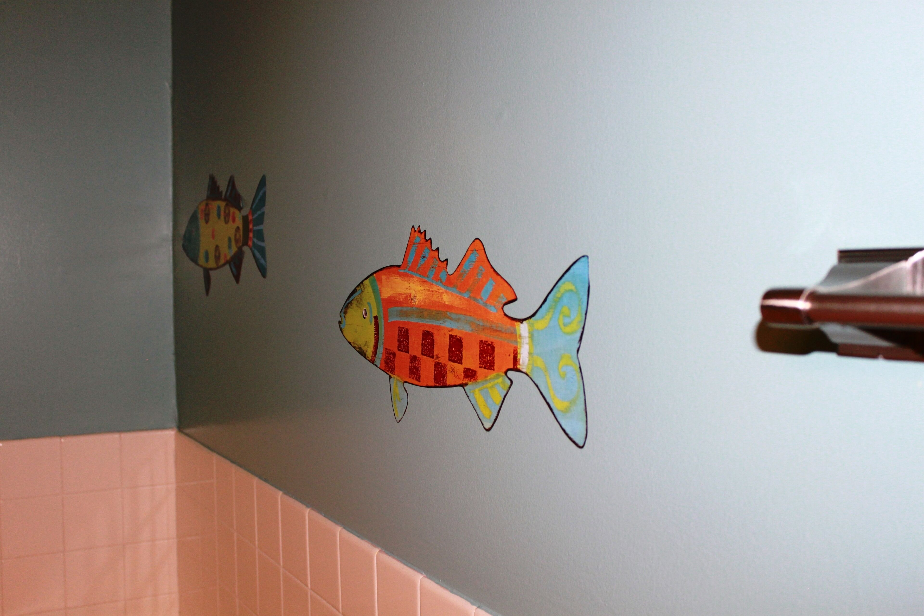 A wall with two fish decals, one larger and one smaller, and a pink tiled area below.