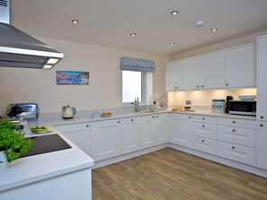 A modern kitchen with white cabinetry, a built-in stove, and a window with a view of the sea.