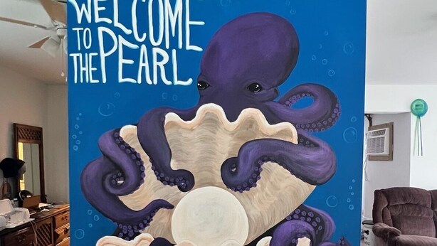 Striscione verticale con una scena subacquea che raffigura un polpo, meduse e coralli, con la scritta 'WELCOME TO THE PEARL'.