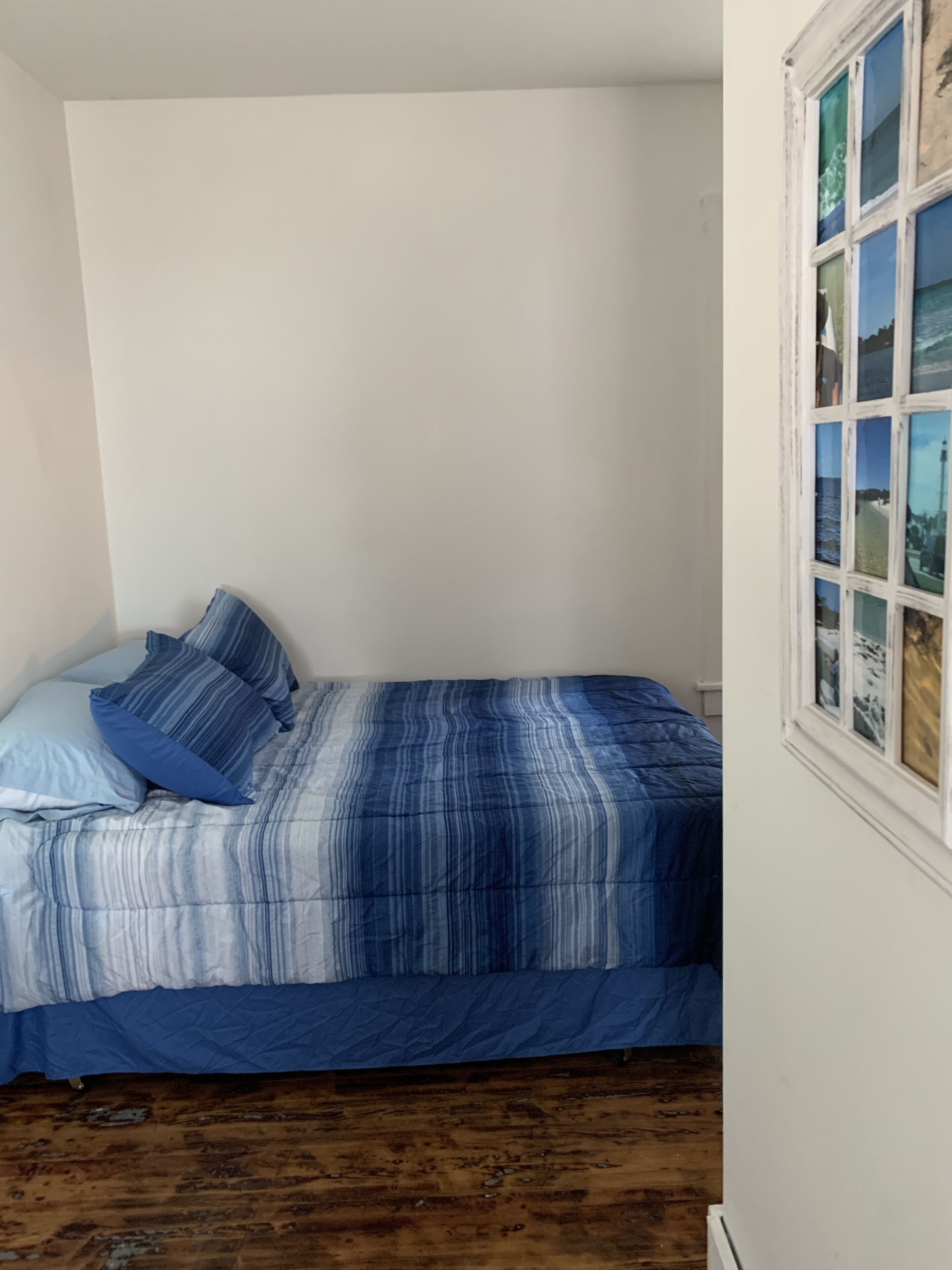 A bedroom with a bed, blue bedding, a wooden floor, and a window with a view.