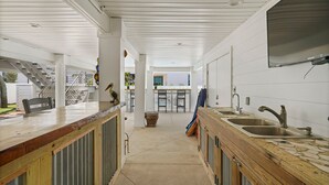 Um corredor estreito e coberto, com um balcão de madeira de um lado e uma área de cozinha com duas pias do outro.