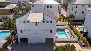 Edifício branco com piscina, cercado por outros edifícios e vista para o oceano.
