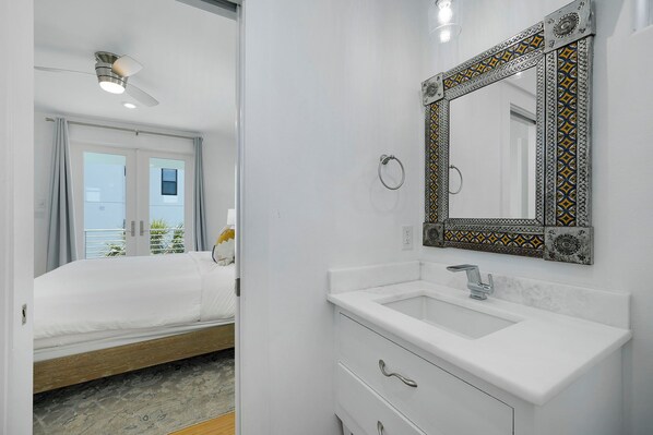 A modern bathroom with a white sink, a mirror with a decorative frame, and a ceiling fan.