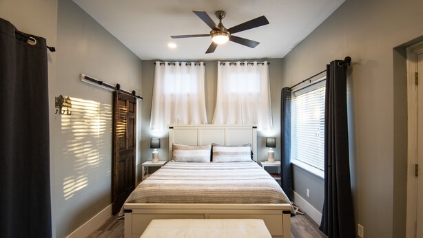 A bedroom with a bed, a ceiling fan, and a window with curtains.