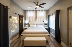 Une chambre à coucher avec un lit, un ventilateur de plafond et une fenêtre avec des rideaux.