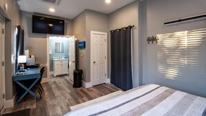 A bedroom with a bed, a desk, and a bathroom in the background.