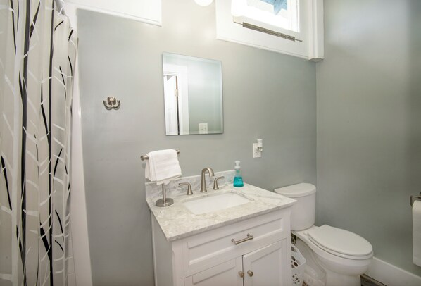 Une salle de bain avec un meuble-lavabo blanc, un évier, un miroir et des toilettes.