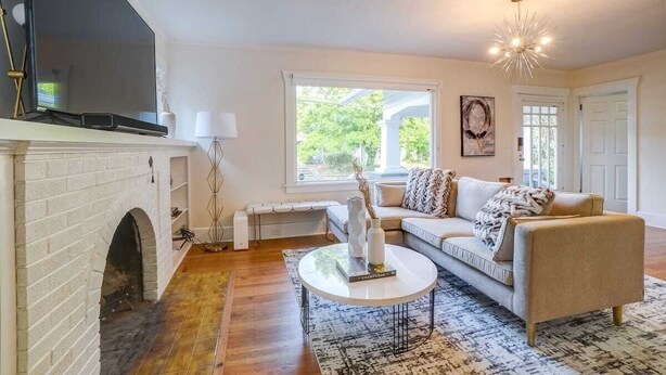 A living room with a fireplace, a sofa, a coffee table, and a chandelier. - Fresh Modern Home in the Alberta Arts District! (Portland)