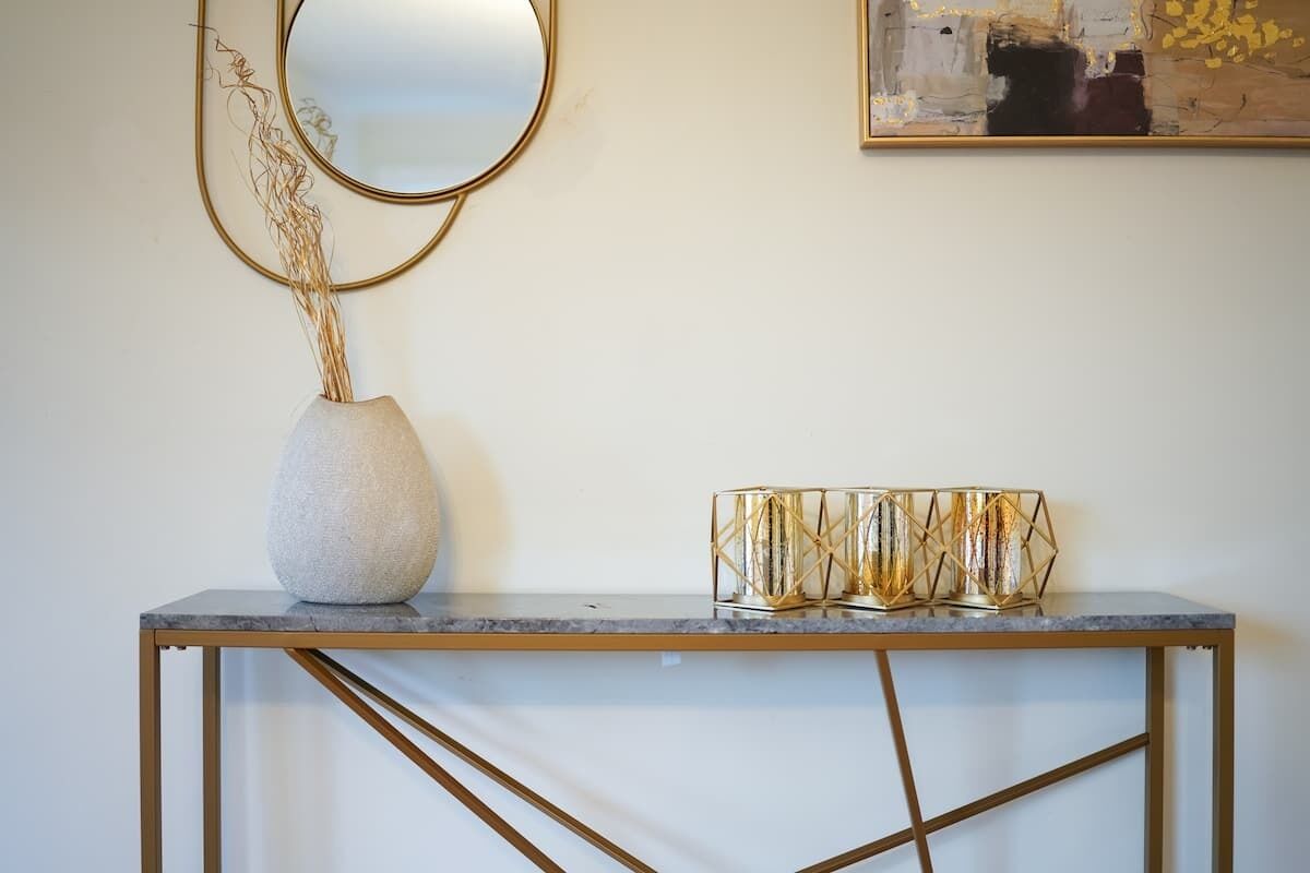 A marble console table with a gold-framed mirror and a decorative vase with dried plants.