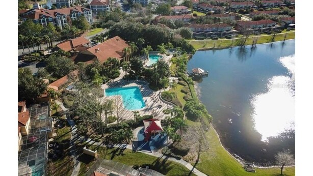 An aerial view of a residential area with a swimming pool surrounded by greenery and a body of water.