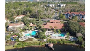 An aerial view of a resort with a central swimming pool, multiple buildings, and surrounding greenery.