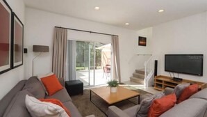 A modern living room with a sofa set, a coffee table, a TV, and a sliding glass door leading to an outdoor area.