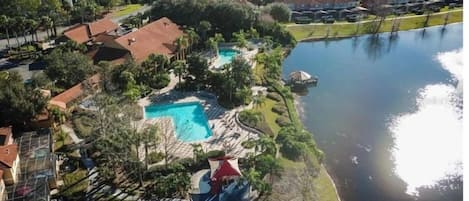 Luftaufnahme einer Wohngegend mit einem Swimmingpool, umgeben von viel Grün und einem Gewässer.
