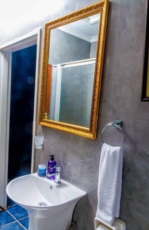 Une salle de bain avec un lavabo blanc, un miroir encadré d’or et un porte-serviettes.
