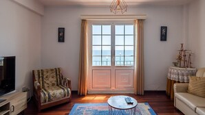 Ein Wohnzimmer mit Fernseher, einer Couch, einem Sessel, einem Couchtisch und Meerblick durch ein großes Fenster.
