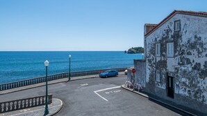 Eine Küstenstraße mit einem blauen Auto am Straßenrand, einem Stoppschild und einem Gebäude mit abblätternder Farbe.