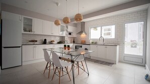 Une cuisine moderne avec des meubles blancs, une table à manger en verre et des luminaires suspendus.