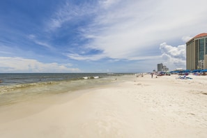 A beach with a hotel in the background, clear skies, and calm sea.