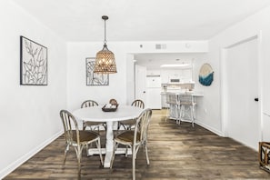 A dining area with a round table and chairs, a hanging light fixture, and framed artwork on the walls.