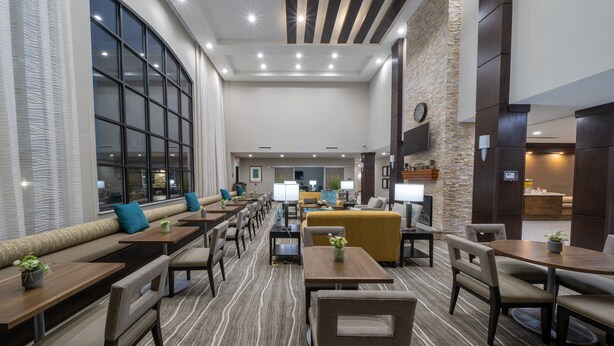 A spacious lobby with a long bench seating area, multiple tables, and a high ceiling with recessed lighting. - Staybridge Suites Houston NW Cypress Crossings by IHG (Houston)