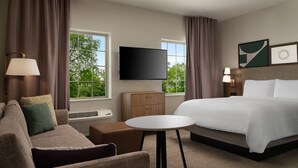 A hotel room with a bed, a sofa, a small table, a TV, and a window with curtains. - Staybridge Suites Houston NW Cypress Crossings by IHG (Houston)