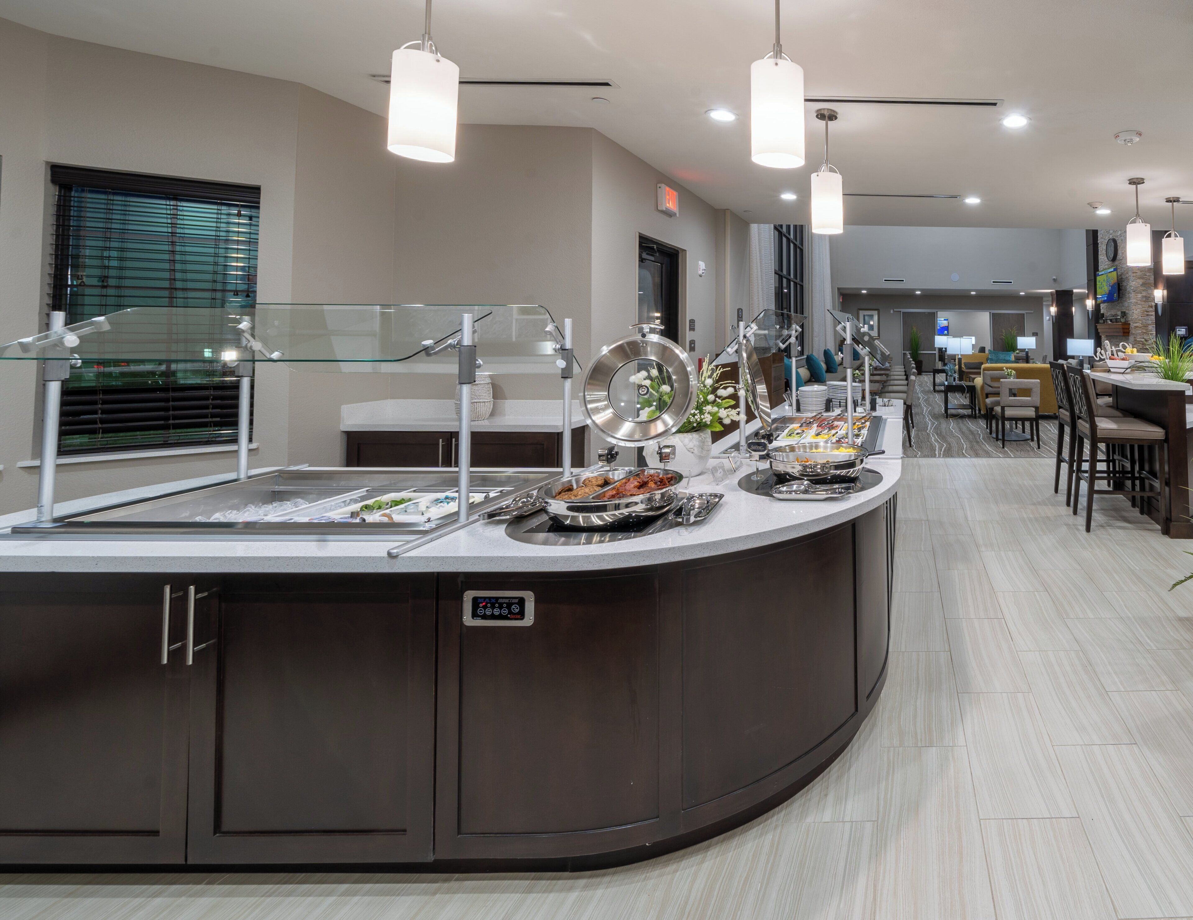 A buffet setup with a variety of food items, a glass display case, and a seating area with tables and chairs.