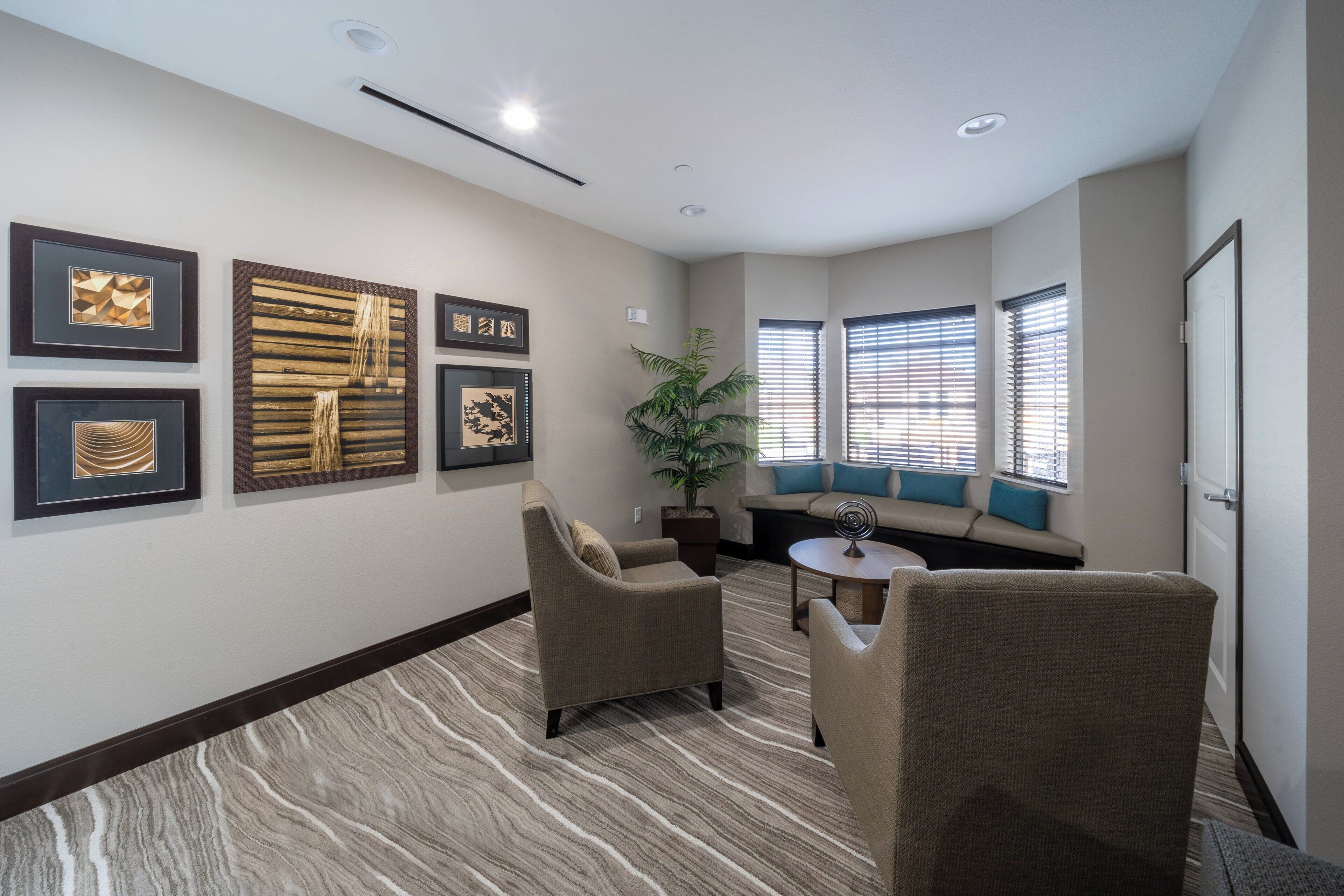 A hotel room with a seating area, a plant, and artwork on the walls.