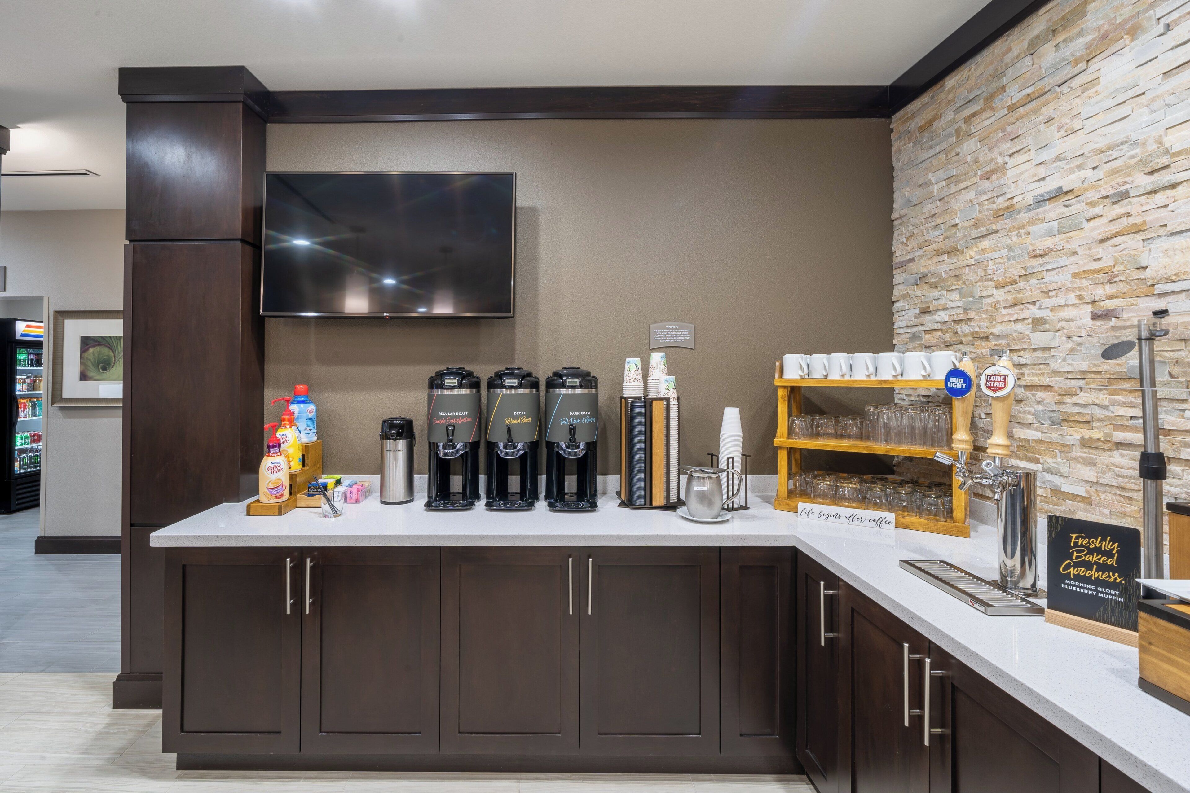 A coffee station with multiple coffee dispensers, a coffee pot, and a sign indicating freshly baked goods.