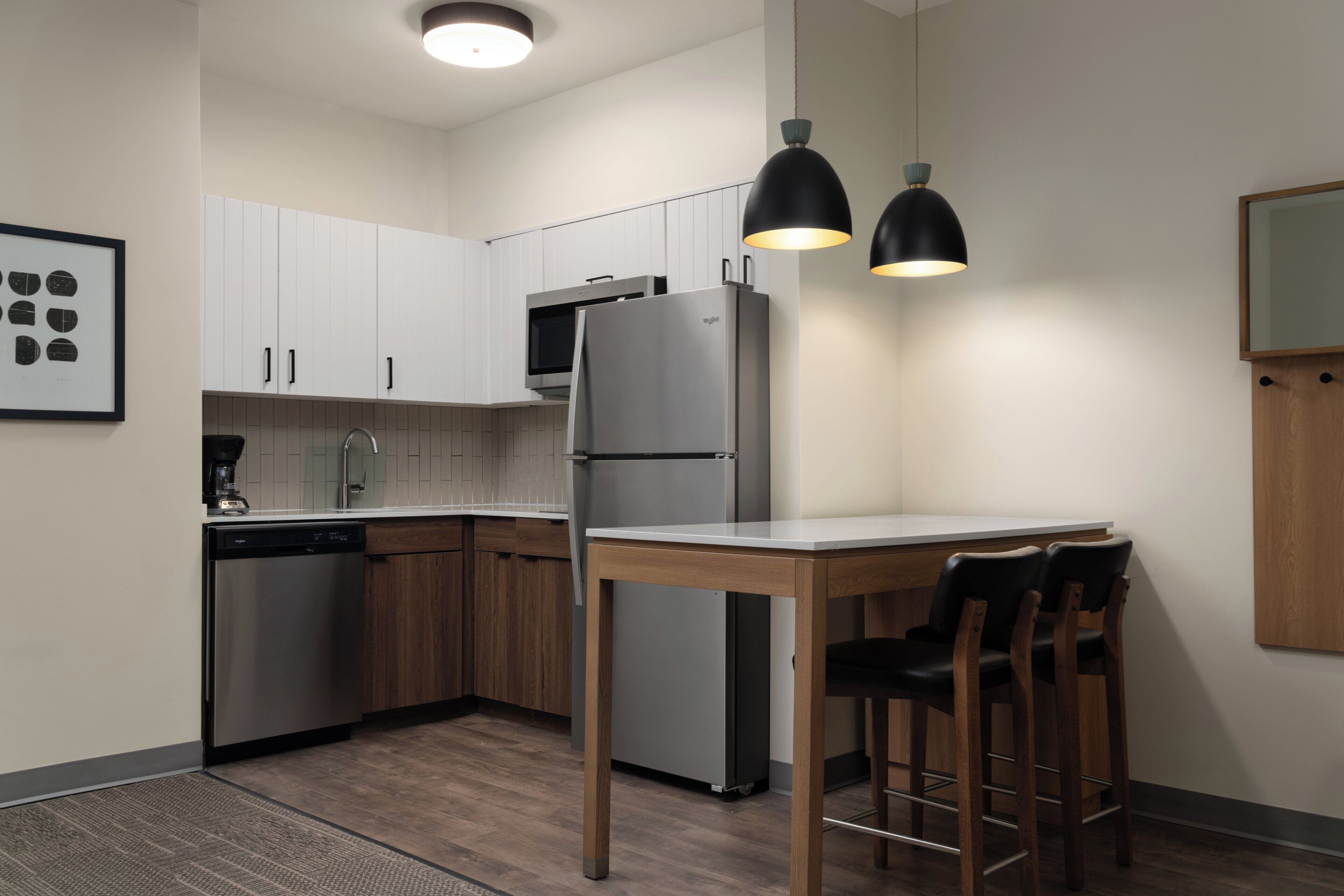 A modern kitchen with white cabinets, a stainless steel refrigerator, a coffee machine, and a dining table with chairs.