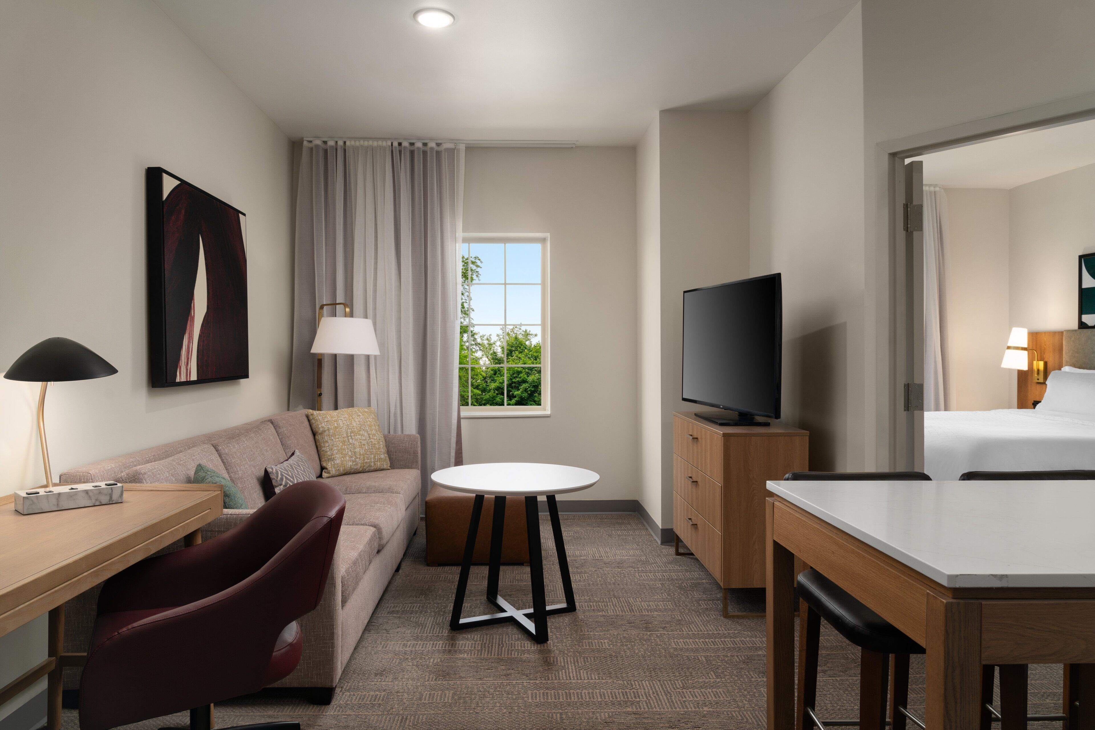 A hotel room with a sofa, a round table, a TV, a bed, and a window with curtains.