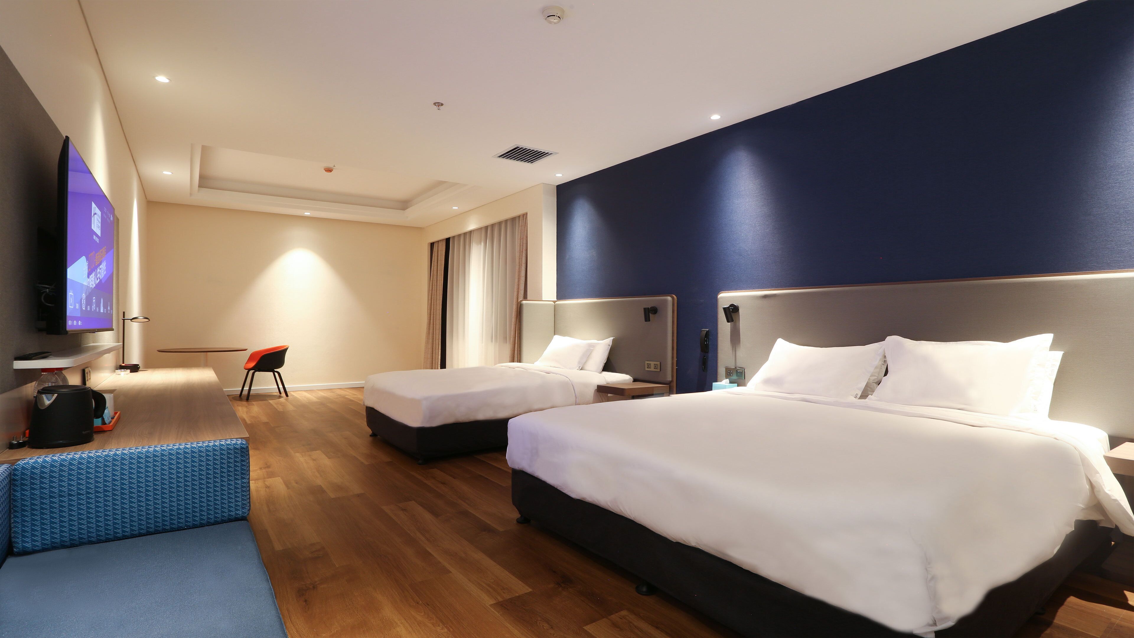 Habitación de hotel con dos camas, un escritorio, una silla, un televisor y una ventana con cortinas.