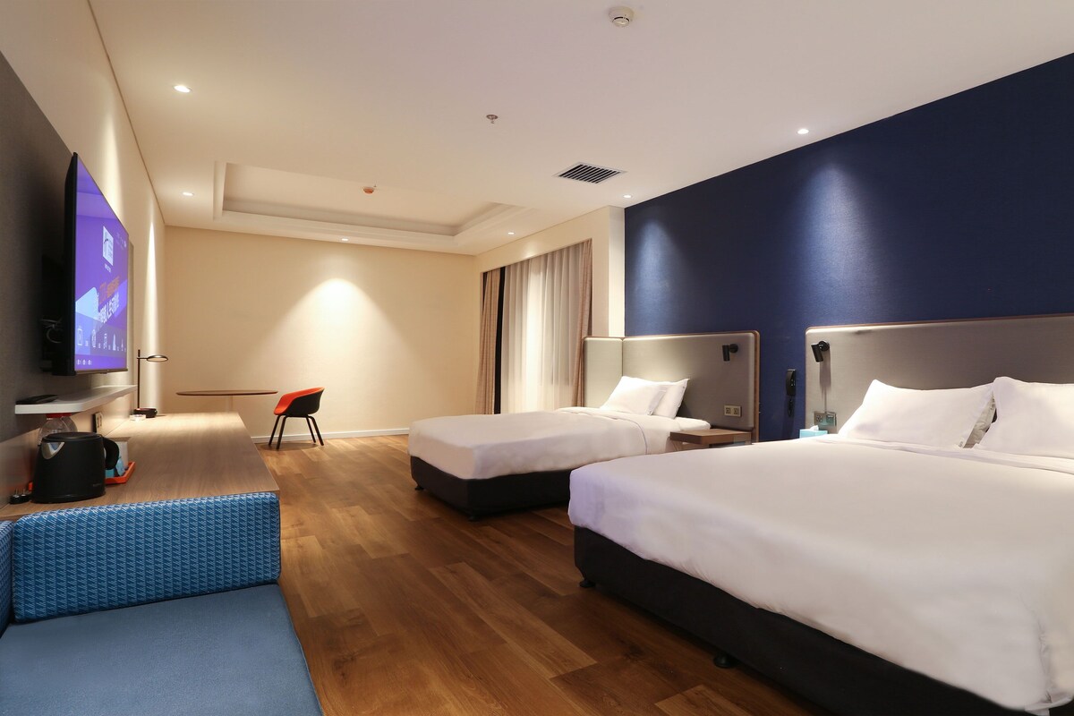 A hotel room with two beds, a desk, a chair, a TV, and a window with curtains.