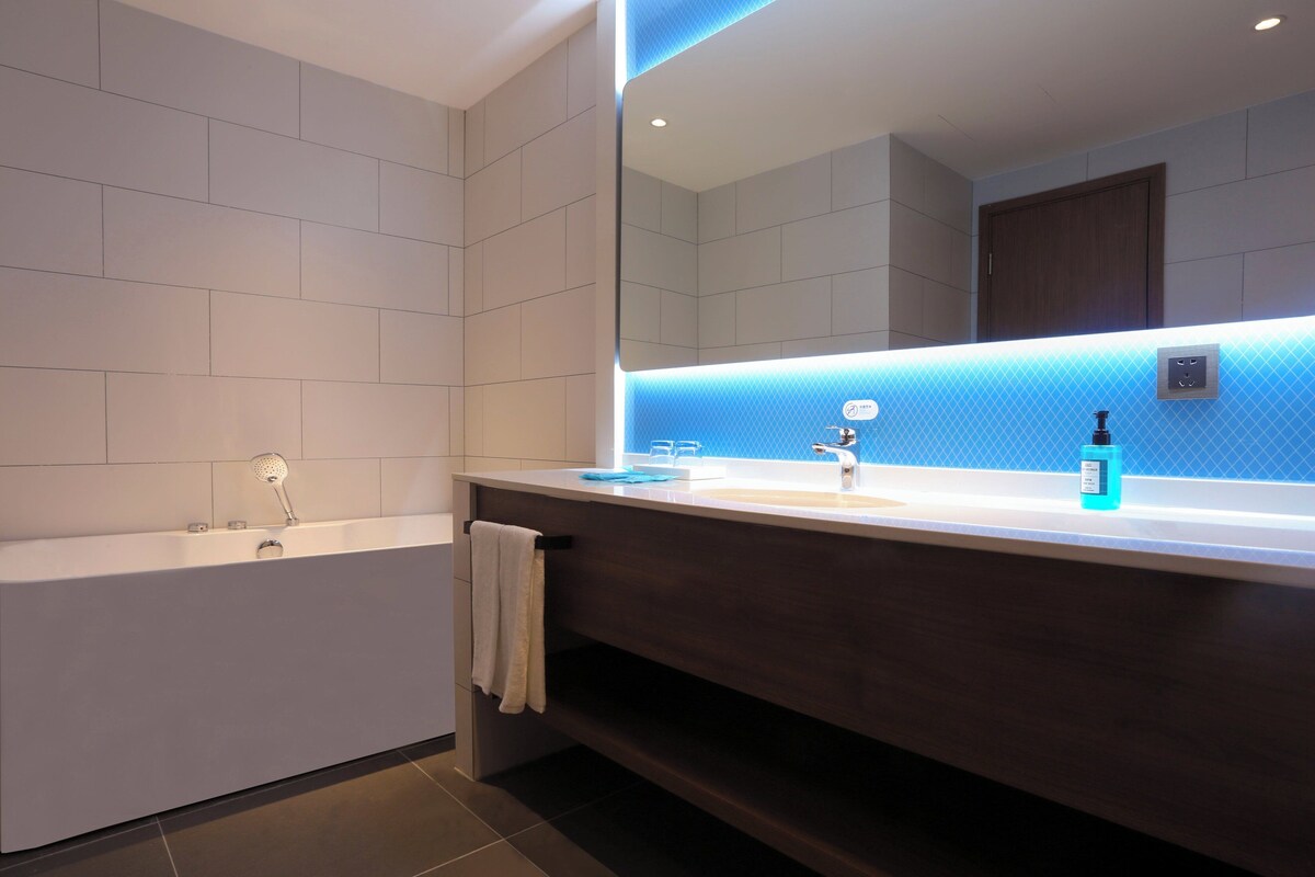A modern bathroom with a bathtub, a large mirror, and a vanity with a sink.